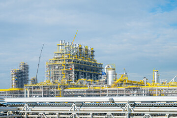 Large industrial chemical plant with metal pipelines and yellow structures under blue sky