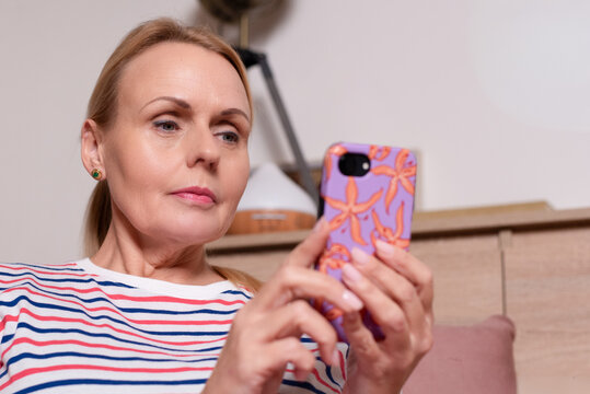Mature woman using smartphone indoors. Concept of modern lifestyle, digital communication, online connection, technology usage and social media interaction at home.