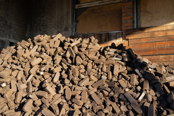 A large pile of wooden blocks is arranged in a rustic environment, with sunlight illuminating the stacks and highlights on the wood