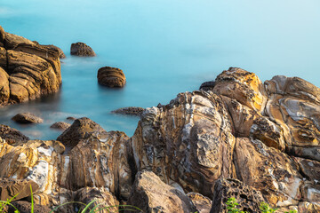 Waves gently splash against the unique sandstone rock formations at Waimushan coastline in Keelung, Taiwan, on a clear summer morning.