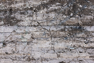Weathered stone and concrete wall displays cracks and rough textures in an urban outdoor setting. Daytime light accentuates the grungy mood of the scene.