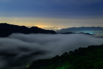 Spectacular night time lapse of a sea of clouds flowing over mountains with city lights glowing in the distance from Jiangmayuan Sanyi Miaoli County Taiwan. © twabian