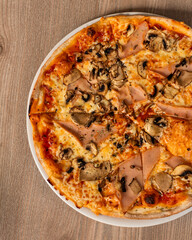 A top view of Pizza capricciosa with tomatoes, greens, mushrooms and cheese on a wooden table