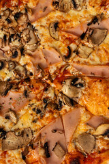 A top view of Pizza capricciosa with tomatoes, greens, mushrooms and cheese on a wooden table