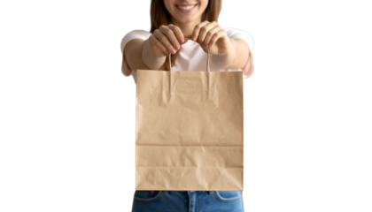 Person in white shirt and jeans smiling, holding a brown paper bag forward