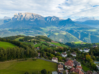Fototapeta premium Aerial view of a scenic alpine village surrounded by green hills and mountains under a bright summer sky, South Tyrol, Italy