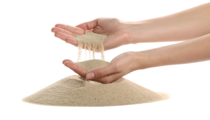 Hands holding and letting fine beige sand fall, forming a pile on a transparent background