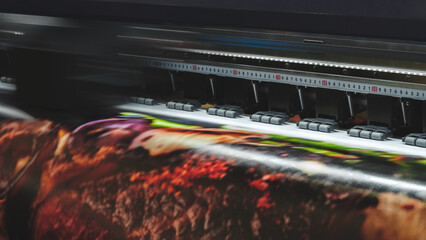 A moving working industrial wide format printer prints a color picture on paper.