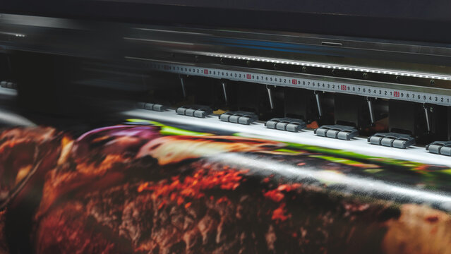 A moving working industrial wide format printer prints a color picture on paper.