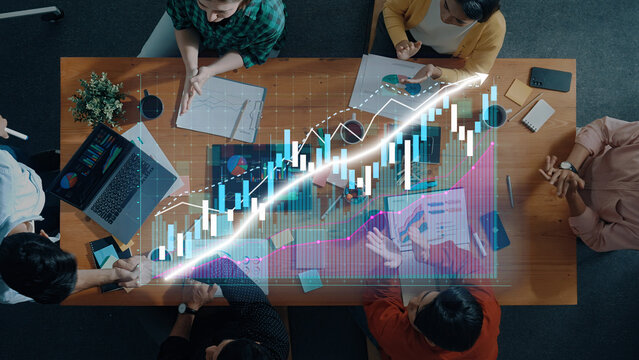 A collaborative business meeting where professionals analyze financial charts and graphs, strategizing and planning in a modern workspace with digital tools. Axiom - Powered by Adobe