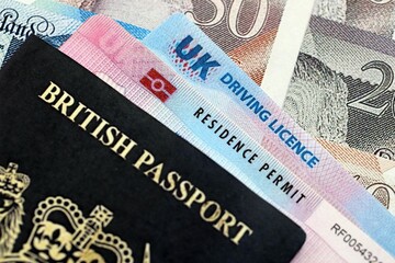 Obraz premium United Kingdom driving license with passport and residence permit card on UK money close up
