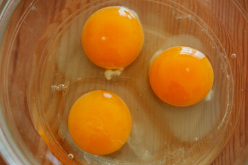 Close-up of raw egg yolks and whites in glass bowl on wood
