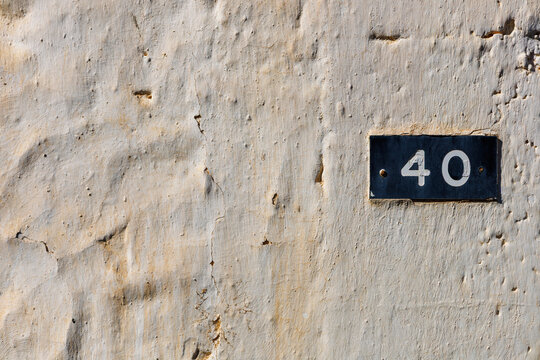 Retro style traditional dark blue nameplate with figures of four and zero. 40 plaque. Enamel house number forty on old light shabby wall. Architectural details. Crete, Greece