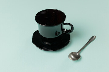 Minimalist Black Coffee Cup with Spoon on Light Teal Background
