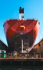 Massive cargo ship under maintenance in dry dock with scaffolding and bright blue sky, industrial maritime scene, shipyard engineering concept.