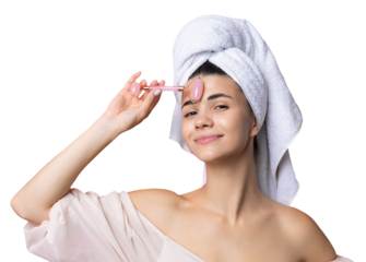 A beautiful cheerful attractive girl with a towel on her head holds a cosmetic roller near her face against a pink background.