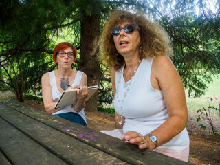 Two women enjoying conversation and art in a park on a sunny day during summer vacation creating memories together