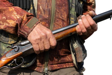 Mature man hunter with gun while walking on field.