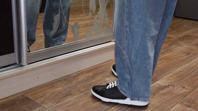 a boy's legs stand in front of a mirror, a boy in front of a mirror dressing room, stands in jeans, a boy gets dressed for school