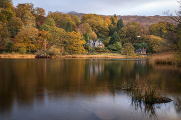 Obraz premium View across a lake in the autumnal Lake District, England, with the foliage colours refecting on the lake