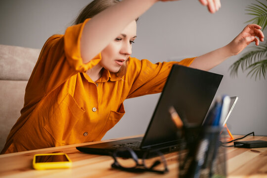 blonde woman in vibrant orange blouse focused on laptop in modern home office engaged in remote work, showcasing blend of professionalism and comfort