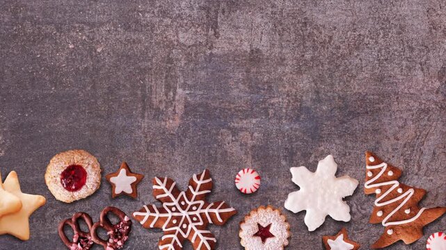 Christmas sweets moving bottom border. Above view, stop motion loop video on a dark stone background with copy space. Gingerbread and a variety of cookies.