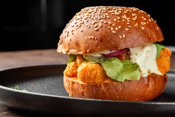 Gourmet fried chicken sandwich on a sesame bun with fresh lettuce, pickled onions, and herb sauce on a dark plate