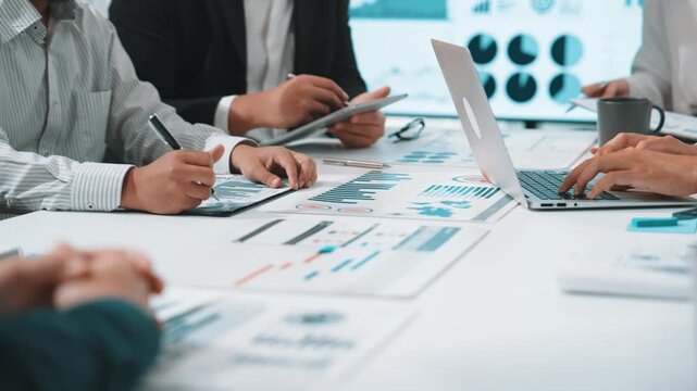 A diverse business team engages in a collaborative financial analysis, surrounded by charts and digital devices while strategizing in a modern office setting. SACTR - Powered by Adobe
