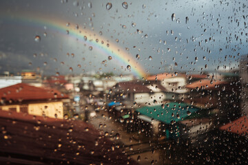 Equatorial Monsoon City Balcony Photovoltaics With Raindrops And Faint Rainbow Over Rooftops, Focus-Pull Look, Afternoon Downpour