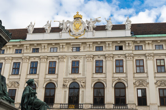 Baroque architectural detail of the Hofburg Palace in Vienna, Austria, with ornate sculptures and a golden imperial crest on the roof