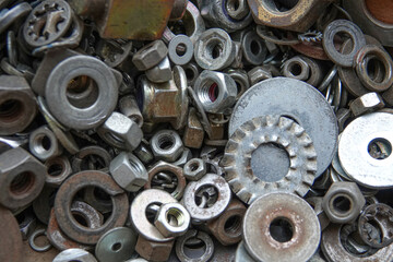 A diverse group of metal nuts, bolts, and washers is spread across a workbench in a garage. Various sizes and shapes show signs of wear from previous use and storage