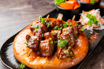Delicious grilled meat skewers (kebabs or satay) served on a round flatbread, garnished with fresh parsley. A savory and appetizing meal on a dark wooden table.