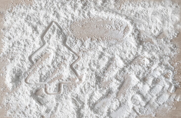 Minimalist holiday baking preparation. A Christmas tree cookie cutter imprint in white flour or powdered sugar. Festive and clean, perfect for winter season food blogs or Christmas sales.