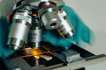 Close-up of scientist???s hands in gloves adjusting microscope focus in sterile lab environment
