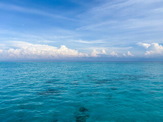 Dreamy turquoise ocean water glistens under a serene blue sky filled with fluffy clouds