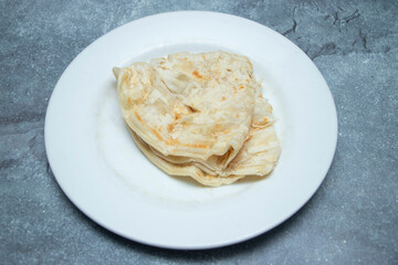 golden and flaky paratha stacked on a white plate, perfect for any meal. Evokes warmth, comfort, and authentic culinary experiences.