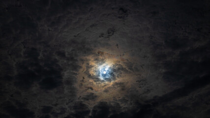 Moon shines through clouds with dramatic blue and gold colored halo 