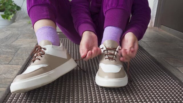 The child sits on the doorstep, tying their shoelaces, little girl sits in sportswear putting on sneakers
