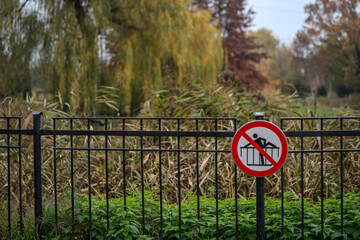 Znak zakazu przechodzenia przez ogrodzenie – symbol ostrzegawczy na metalowej barierce w parku © Kacper