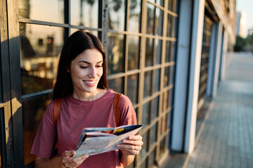 Fototapeta premium Portrait of a smiling young woman looking at a map in the city, tourists visiting destination, summer trip exploring