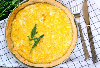 Golden homemade quiche with melted cheese and a crispy crust, garnished with fresh arugula. Freshly baked cheese quiche. Top view.