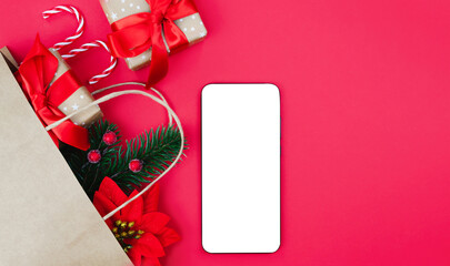 Smartphone with blank screen, Christmas gifts and decorations on red background. Festive composition for online shopping, social media or holiday greetings. Close-up. Copy space.