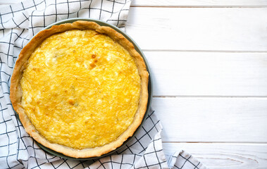 Homemade cheese quiche on a wooden background. Savory pie with golden crust and melted cheese, placed on a checkered kitchen towel. Top view. Copy space.