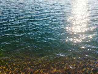 View of calm water with clear shoreline and sunlit path on water surface, serene landscape scene with copy space