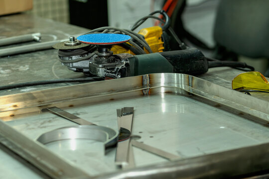 Metal workshop table with grinder, safety glasses and stainless steel parts. - Powered by Adobe