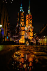 Illuminated cathedral of St John the Baptist in Wroclaw, Poland, reflected in puddle at night with festive lights. Concept of architecture and travel destination