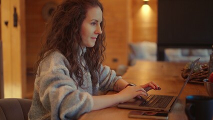 Portrait of middle aged woman sitting at desk. Businesswoman remote working on laptop in home office. Female wearing turtleneck pullover. . Autumn or winter indoor clothing .