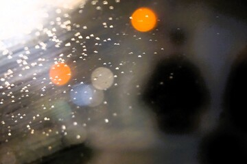 Abstraktes Motiv mit orange-braungrauen Lichtern vor schwarzem Mann auf Gehweg in Stadt in der Nacht bei Sturm, Frost und Regen im Winter