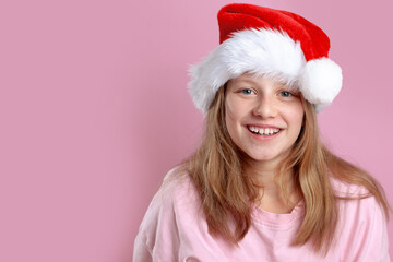 Excited pretty 11-year-old girl in pink T-shirt and Santa hat posing on pink background