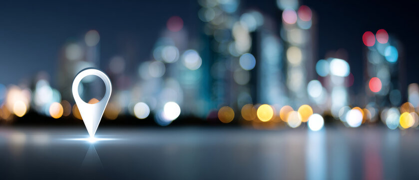 Glowing location pin icon on reflective surface with blurred city skyline and colorful bokeh lights in background at night